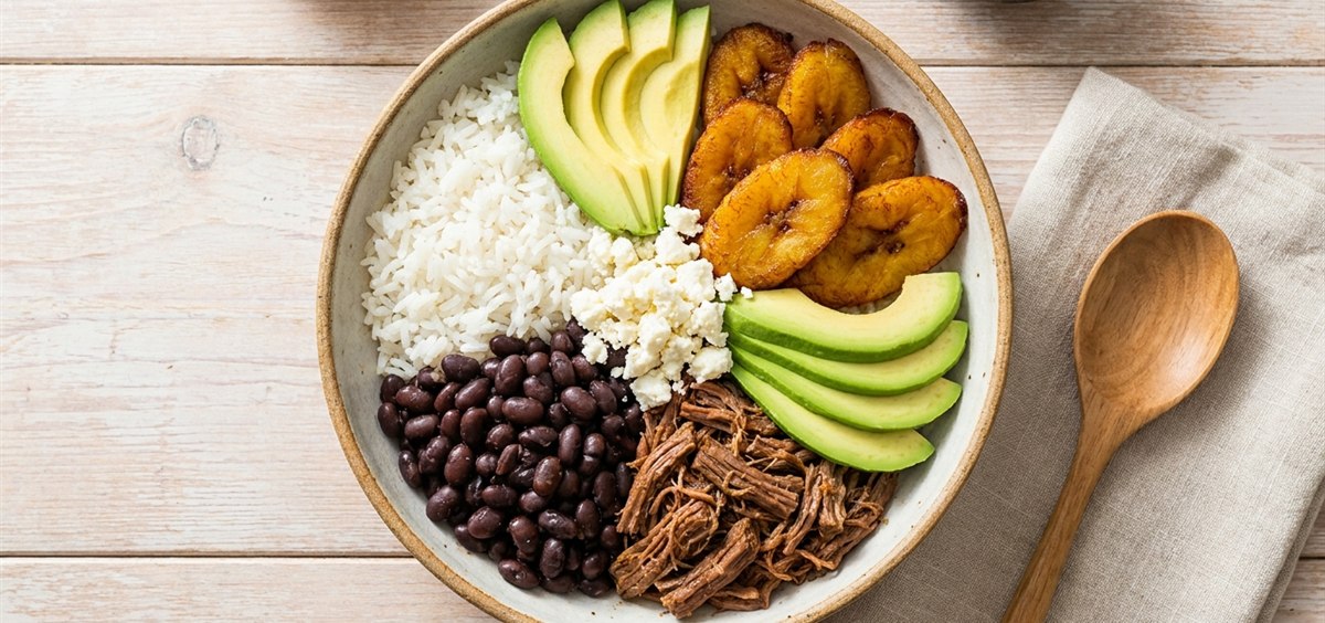Overhead view of a modern Venezuelan bowl with rice, black beans, shredded beef, sweet plantains, white cheese and avocado